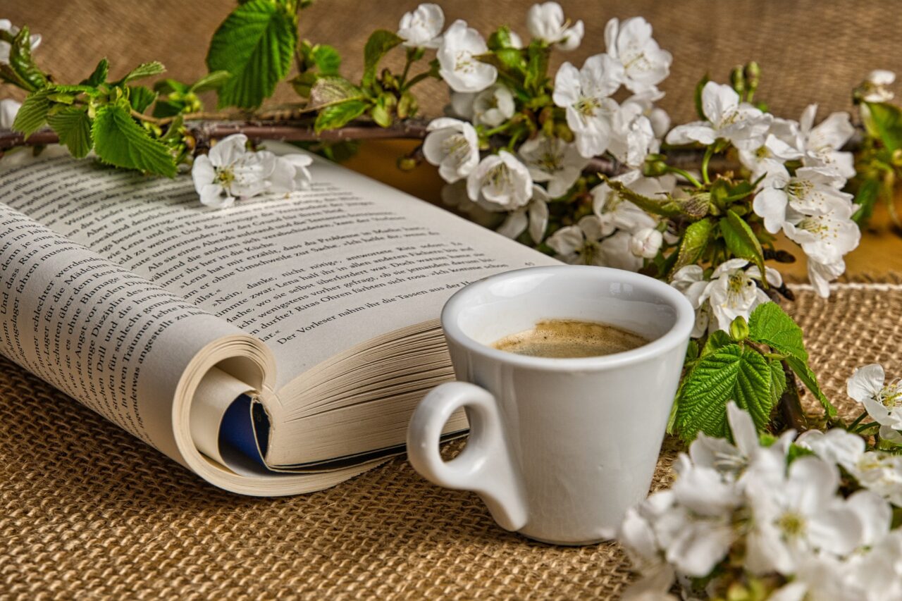 Uppslagen bok, blommande kvist och en kaffekopp